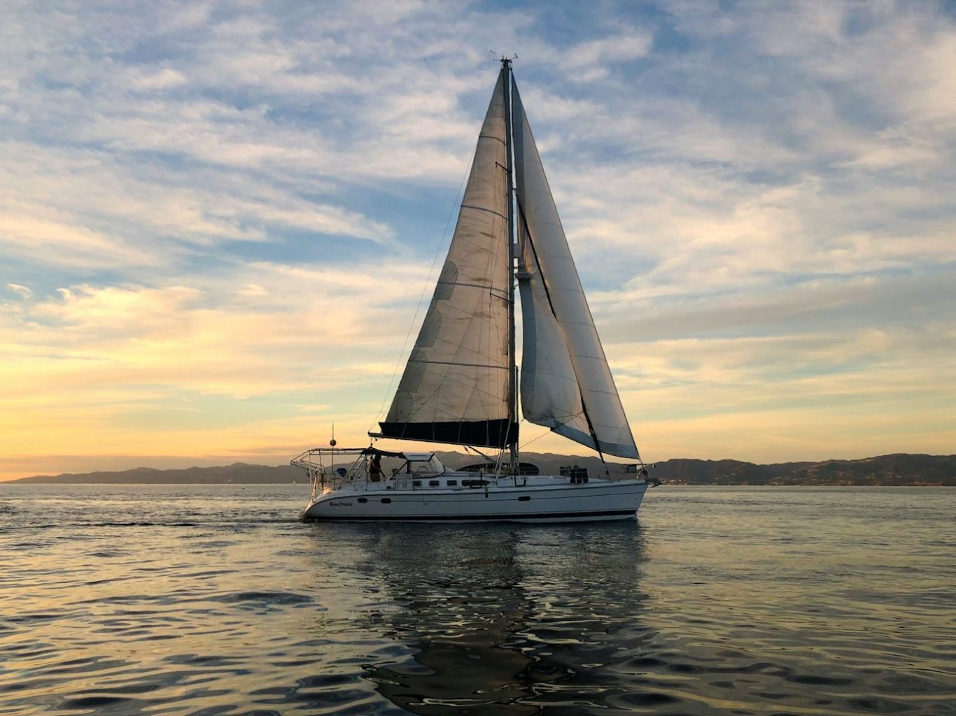 Un voilier naviguant sur des eaux calmes au crépuscule, avec des voiles déployées et son revêtement de pont.