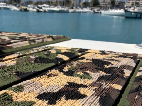 Tapis camouflé sur un quai avec yachts en arrière-plan.