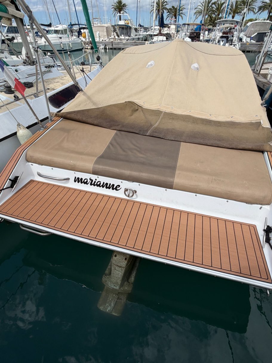 Bateau amarré avec un pont en effet teck et une toile de protection beigne.
